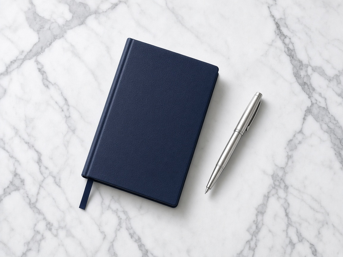 Navy notebook and silver pen on white marble
